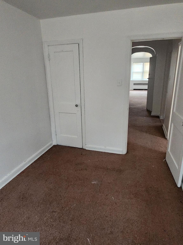 empty room featuring arched walkways, baseboards, and dark colored carpet
