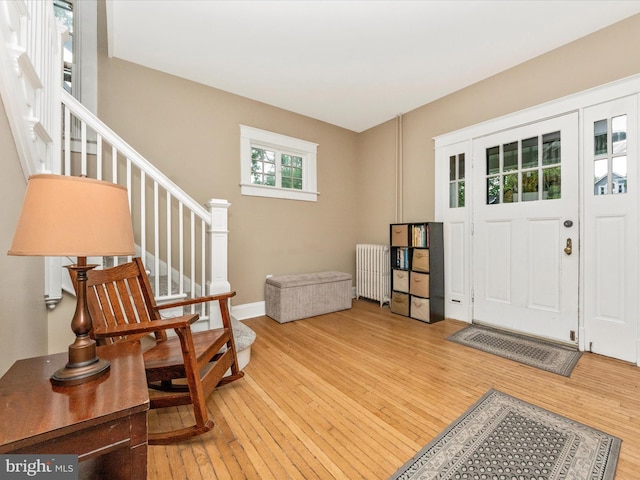 foyer entrance featuring stairway, baseboards, light wood-type flooring, and radiator heating unit