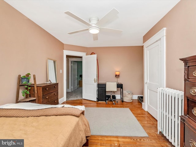 bedroom featuring radiator, light wood-type flooring, baseboards, and ceiling fan