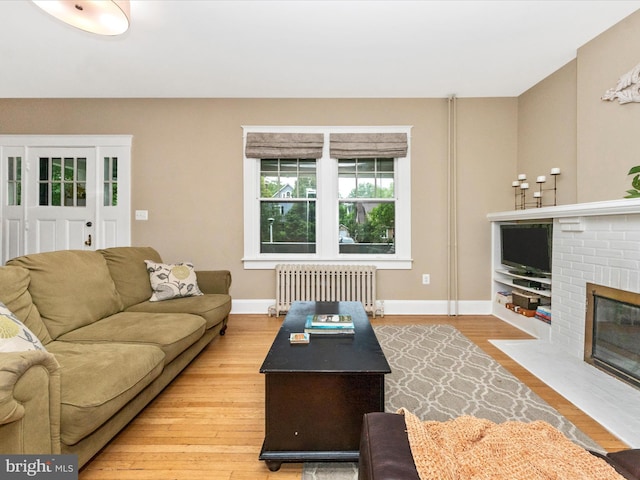 living room with a brick fireplace, baseboards, light wood-type flooring, and radiator heating unit