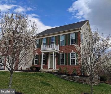 colonial-style house featuring brick siding, a front yard, and a balcony