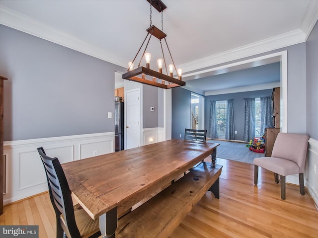 dining room with light wood-type flooring, crown molding, a decorative wall, a chandelier, and wainscoting