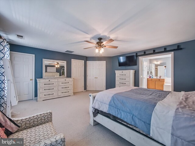 bedroom with carpet floors, two closets, ensuite bathroom, a ceiling fan, and a barn door