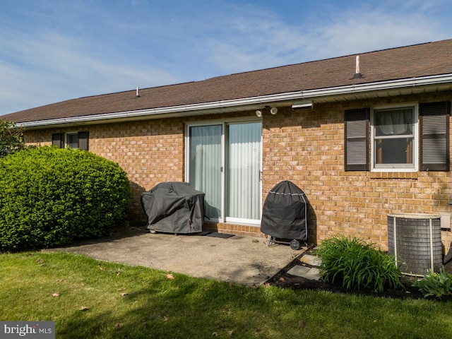 rear view of property featuring central AC unit, a patio area, brick siding, and a yard