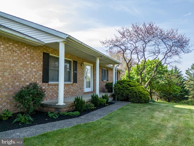 view of side of home with a lawn, a porch, and brick siding