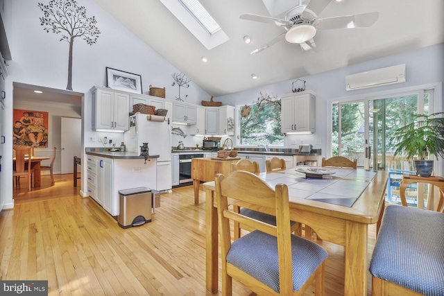 dining area with high vaulted ceiling, ceiling fan, light wood-style flooring, and a wall mounted air conditioner