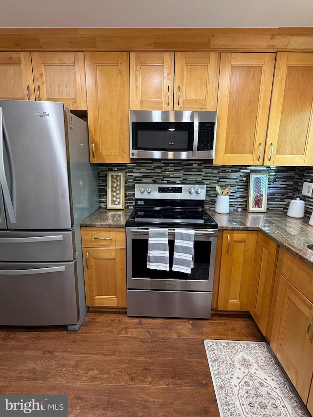 kitchen featuring dark wood-style floors, stainless steel appliances, dark stone countertops, and decorative backsplash