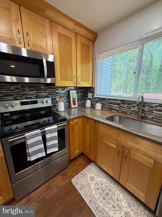 kitchen featuring a sink, dark stone countertops, decorative backsplash, stainless steel appliances, and dark wood-style floors