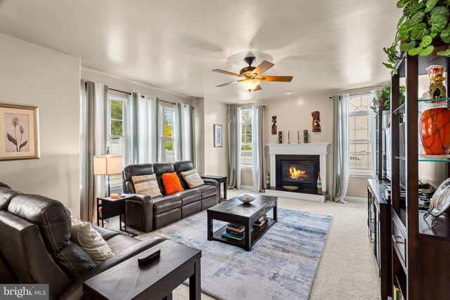 living area with a ceiling fan, a glass covered fireplace, and carpet floors