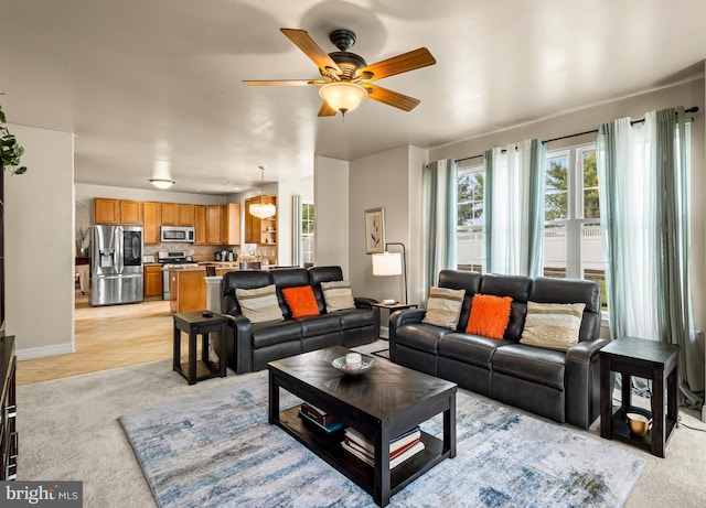 living area with light colored carpet, light tile patterned floors, baseboards, and ceiling fan