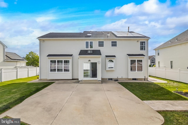 rear view of property featuring a patio, solar panels, a lawn, and fence