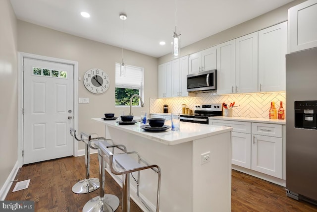 kitchen with stainless steel appliances, a breakfast bar area, backsplash, dark wood-style floors, and a kitchen island