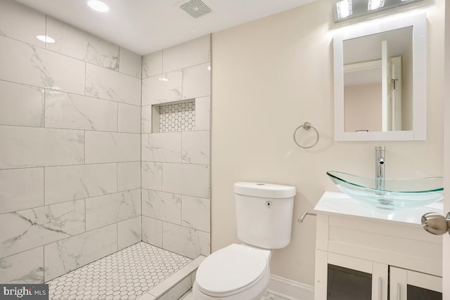 bathroom with toilet, baseboards, visible vents, tiled shower, and vanity