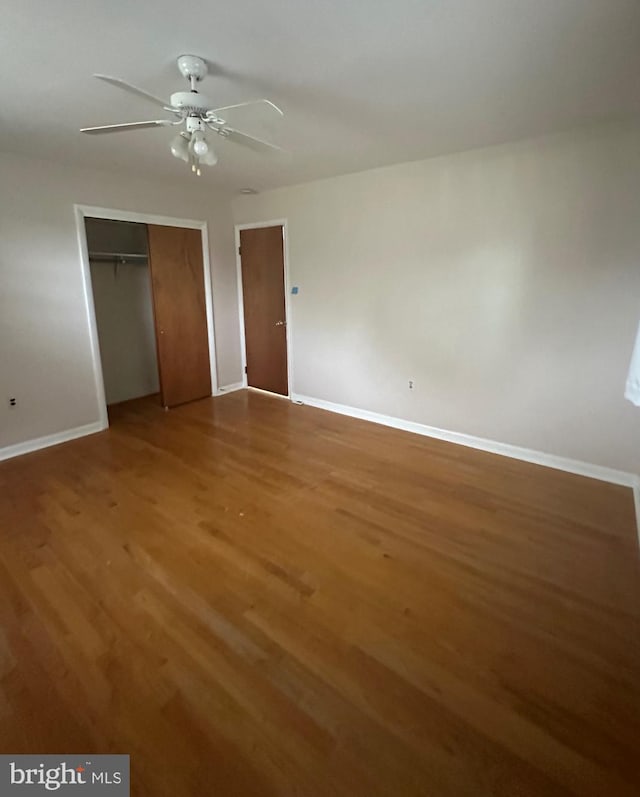 unfurnished bedroom with wood finished floors, baseboards, a closet, and a ceiling fan