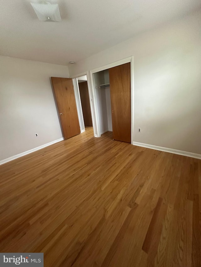 unfurnished bedroom with baseboards, wood finished floors, and a closet