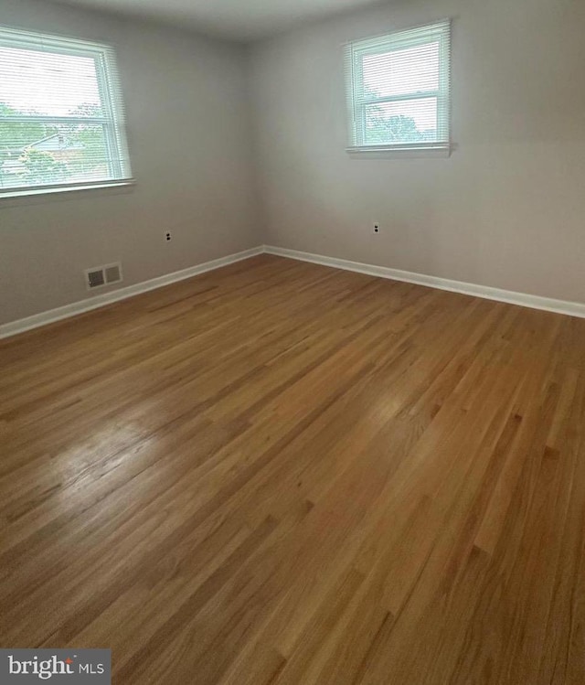 empty room featuring plenty of natural light, wood finished floors, and baseboards
