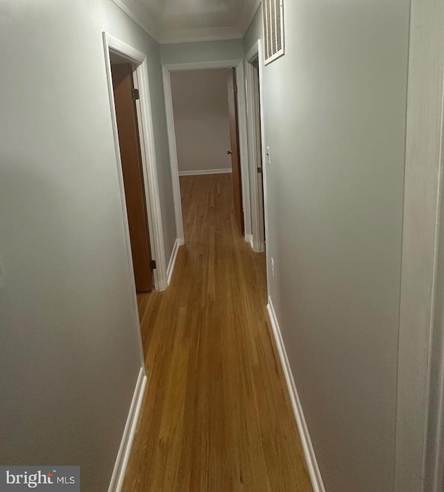 corridor with light wood-style flooring, crown molding, and baseboards