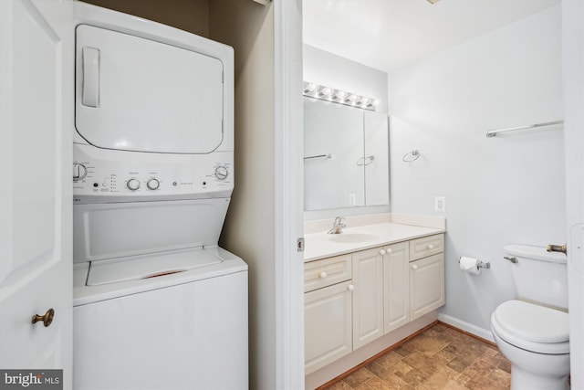 bathroom featuring toilet, stacked washer / dryer, vanity, stone finish floor, and baseboards