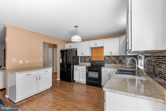 kitchen with black appliances, a sink, backsplash, light wood finished floors, and light countertops