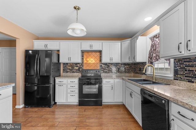 kitchen featuring black appliances, a sink, light wood-type flooring, decorative light fixtures, and tasteful backsplash