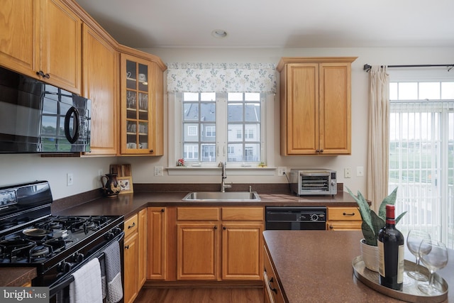kitchen featuring a sink, black appliances, a toaster, glass insert cabinets, and dark countertops