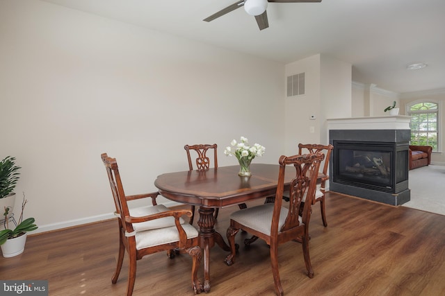 dining area with wood finished floors, a multi sided fireplace, visible vents, baseboards, and ceiling fan