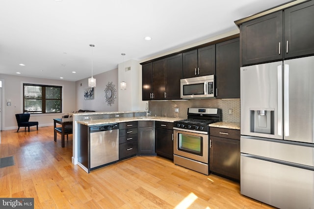 kitchen featuring tasteful backsplash, decorative light fixtures, light wood finished floors, light stone countertops, and appliances with stainless steel finishes