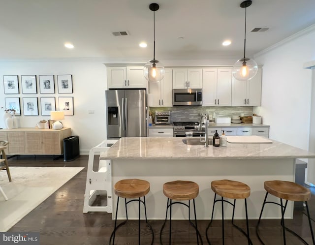 kitchen with stainless steel appliances, a breakfast bar, white cabinetry, decorative backsplash, and ornamental molding
