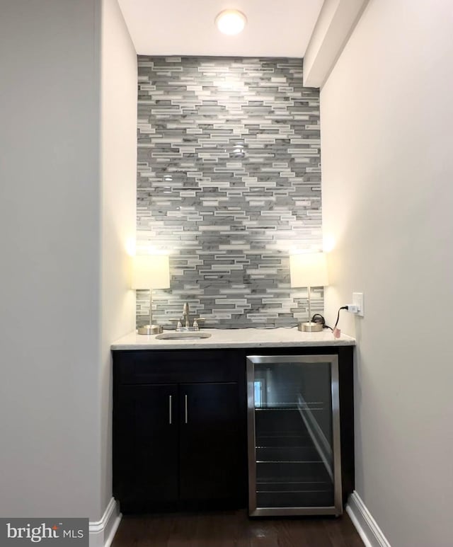 indoor wet bar featuring wine cooler, dark wood-style flooring, decorative backsplash, and baseboards