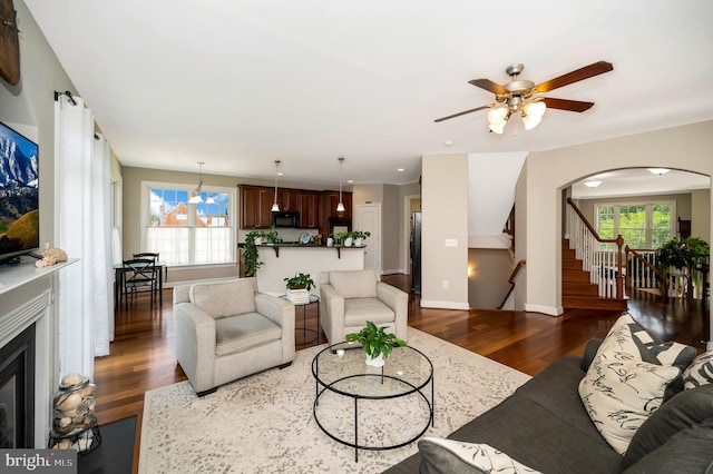 living room with wood finished floors, ceiling fan, stairs, a glass covered fireplace, and baseboards