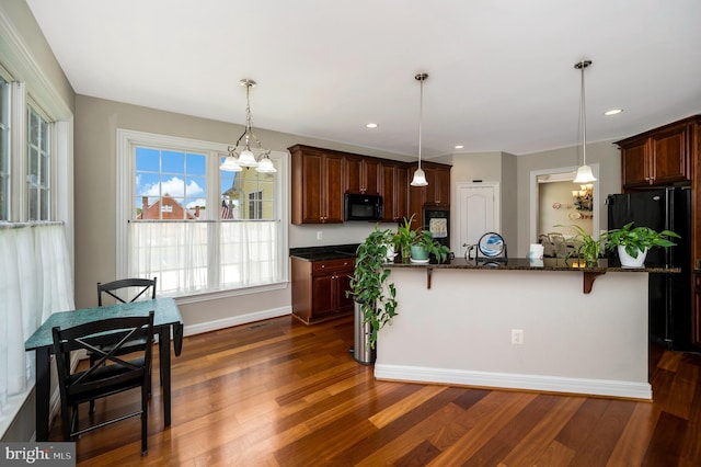kitchen with black appliances, dark wood finished floors, a kitchen breakfast bar, pendant lighting, and dark stone countertops