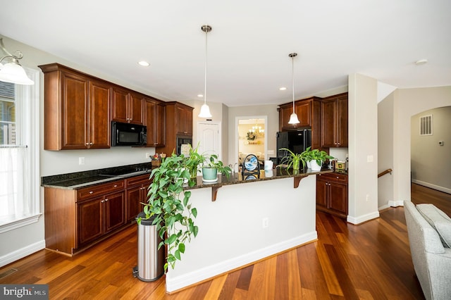 kitchen with black appliances, a breakfast bar, arched walkways, dark stone counters, and dark wood-type flooring