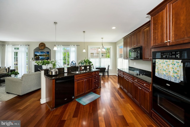 kitchen with black appliances, dark wood-type flooring, decorative light fixtures, a sink, and dark stone countertops