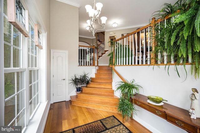 stairway with crown molding, wood finished floors, a chandelier, and baseboards