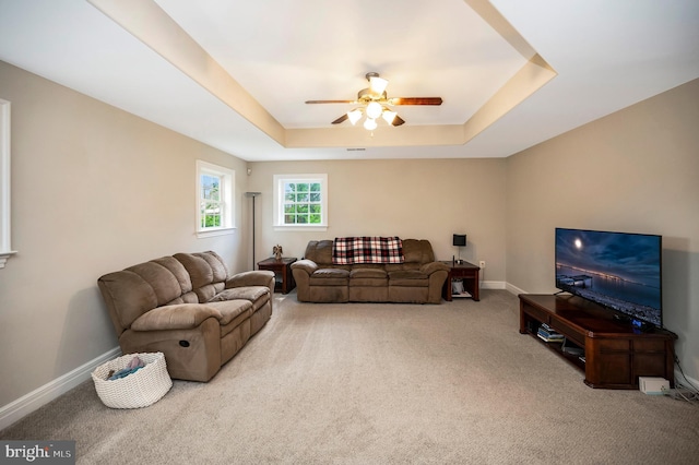 living room with a raised ceiling, a ceiling fan, carpet, and baseboards