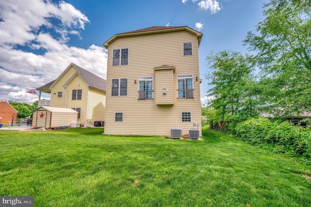 rear view of property featuring cooling unit, a storage shed, an outdoor structure, and a lawn