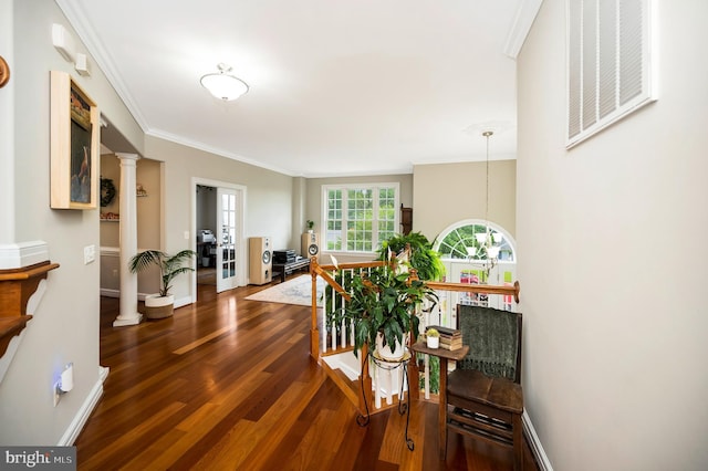 hall featuring wood finished floors, decorative columns, ornamental molding, baseboards, and an upstairs landing