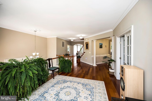 foyer featuring dark wood-style flooring, ornamental molding, baseboards, a chandelier, and ornate columns