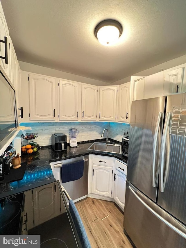 kitchen with a sink, white cabinetry, dark countertops, stainless steel appliances, and light wood-type flooring