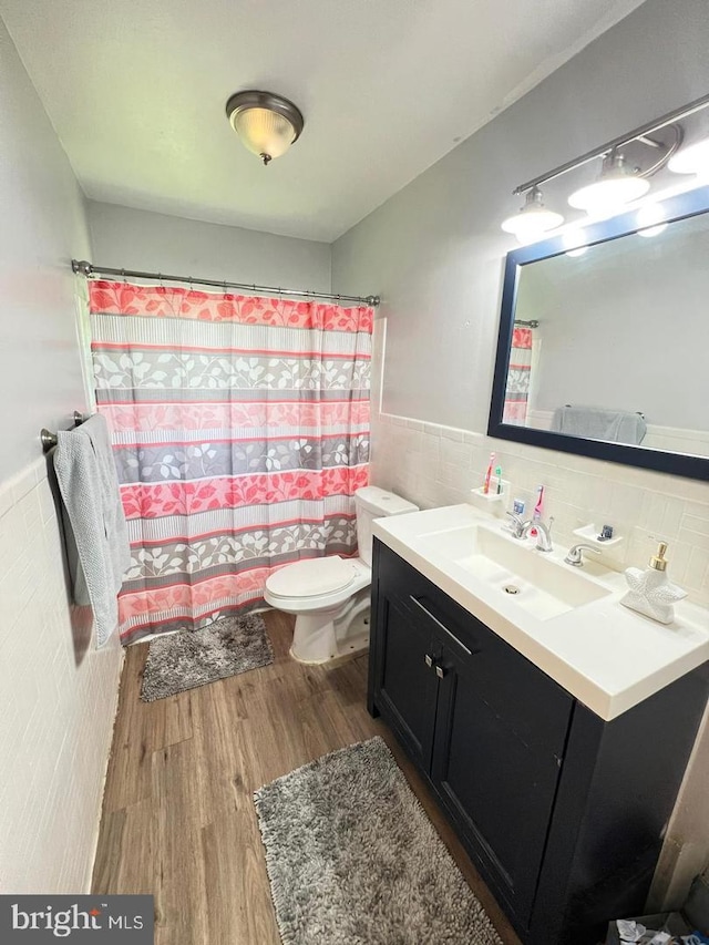 bathroom with tile walls, toilet, a wainscoted wall, wood finished floors, and vanity