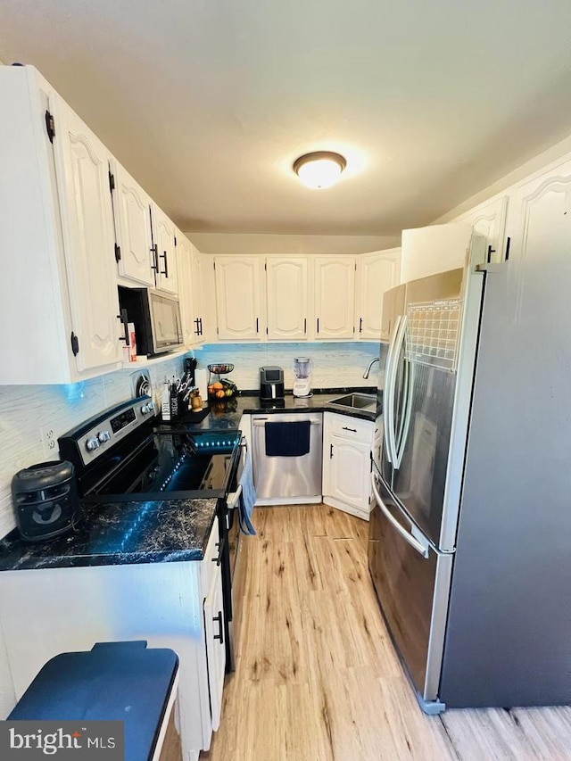 kitchen with a sink, stainless steel appliances, backsplash, white cabinets, and light wood-style floors