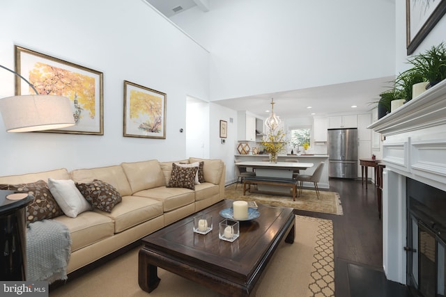 living room featuring a fireplace, dark wood-type flooring, visible vents, a towering ceiling, and a chandelier