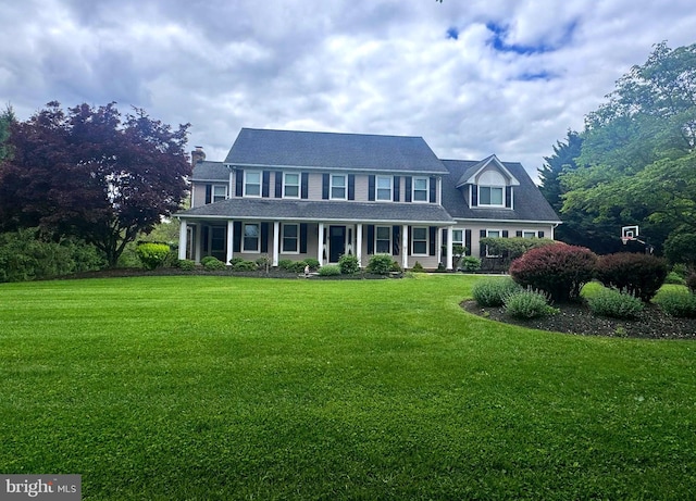 colonial inspired home featuring a front yard, covered porch, and a chimney