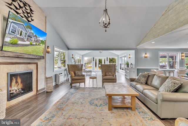 living area featuring lofted ceiling, a tile fireplace, an inviting chandelier, and wood finished floors