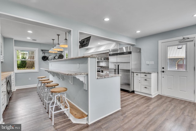 kitchen with light stone counters, built in fridge, a kitchen breakfast bar, wood finished floors, and white cabinets