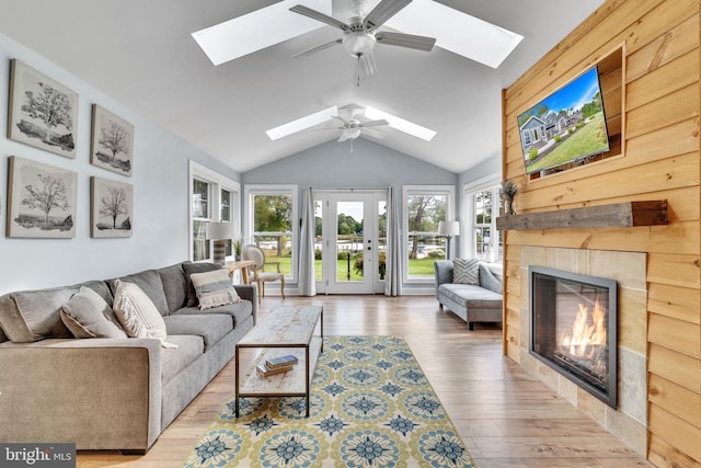 living area with vaulted ceiling with skylight, a ceiling fan, a tiled fireplace, and wood finished floors