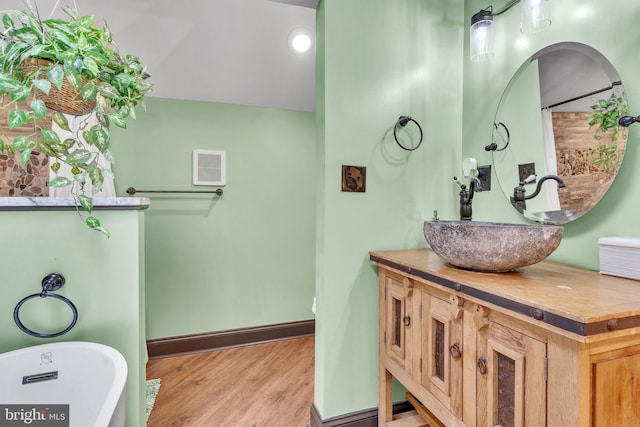 full bathroom with baseboards, vanity, a freestanding tub, and wood finished floors
