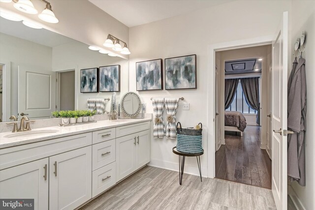 ensuite bathroom featuring double vanity, baseboards, and wood finished floors