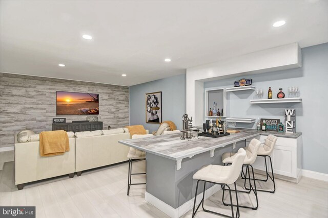 kitchen with an accent wall, a breakfast bar, recessed lighting, baseboards, and light wood finished floors
