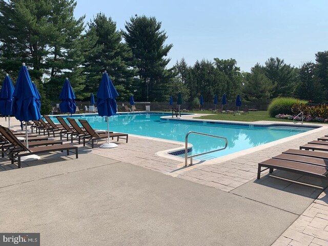 community pool with a patio, fence, and view of wooded area